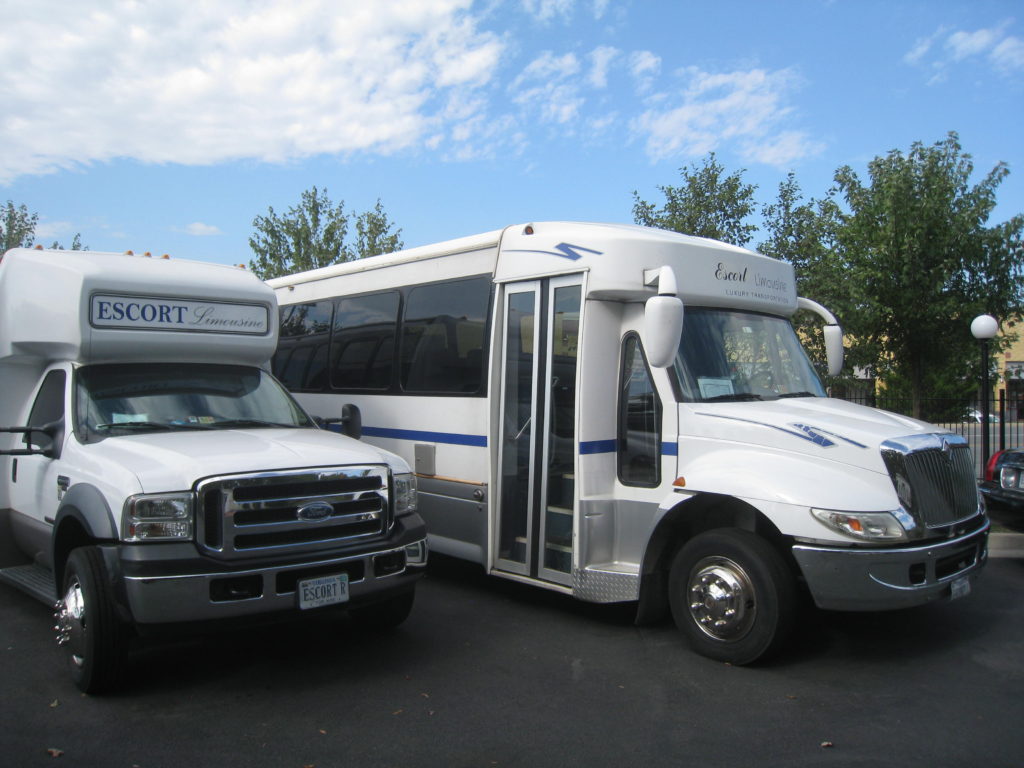 A white bus and truck parked in a parking lot.