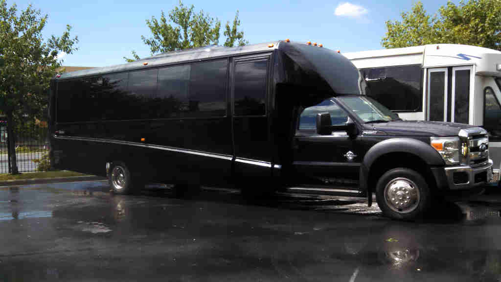 Black luxury bus parked on wet pavement.
